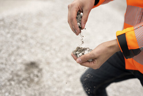 Betongranulat auf einem Haufen, ein Mann in orangener Jacke bewegt das Granulat zwischen den Händen