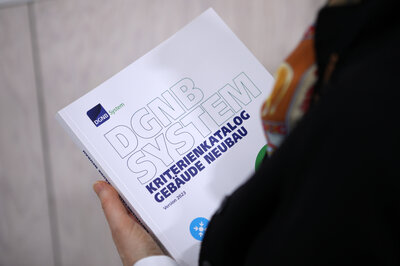 Neue Version 2023 des DGNB Systems für Neubauten: fotografiert über die Schulter einer Person, die die neue Version ausgedruckt in den Händen hält