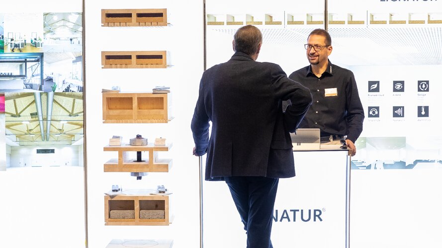 Stand auf dem 26. Internationalen Holzbau-Forum - ein Besucher im Gespräch mit einem Standmitarbeiter