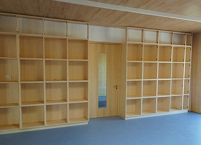 Innenraum der Betreuungseinrichtung: Holzregale bis unte die Decker, blauer Fußboden