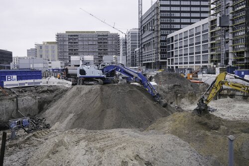 Natürlich-gewachsener Boden weicht einem Neubauvorhaben. Im Hintergrund stehen LKW für den Abtransport des Aushubs bereit.