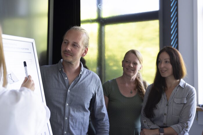 Drei Seminarteilnehmer stehen neben einem Flipchart