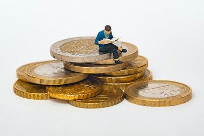 Männliche Figur auf einem Münzhaufen sitzend