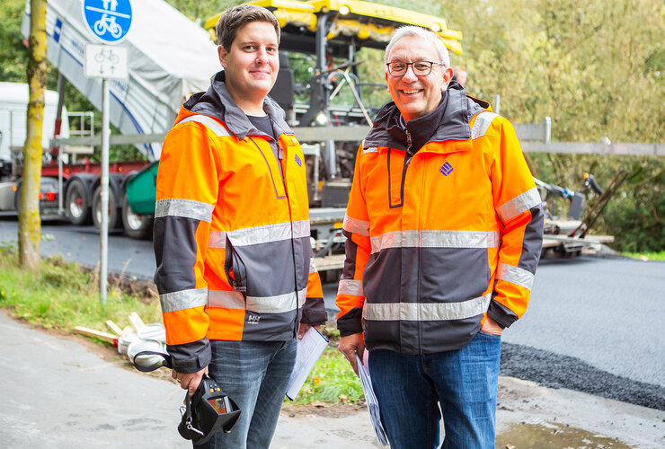 Prof. Dr. Hans-Hermann Weßelborg (r.) und Thomas Schönauer in orangefarbenen Warnjacken vor der Teststrecke zum Asphaltstraßenbau in Münster