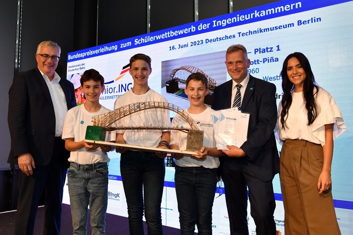 Preisverleihung Schülerwettbewerb Junior.ING der Ingenieurkammern: Hendrik Dresen, Linus Dresen und Christian Bode des Freiherr-vom-Stein-Gymnasiums (Oberhausen) erhielten in der Alterskategorie bis Klasse 8 des Schülerwettbewerbs den ersten Preis für ihr Brückenmodell "Ruhrpott-Piña". Der Vizepräsident der Bundesingenieurkammer, Ingolf Kluge (links), und der Juryvorsitzende des Landeswettbewerb Nordrhein-Westfalen, Georg Wiemann, überreichten den Schülern gemeinsam mit der Moderatorin Jessica Schöne die Urkunden.