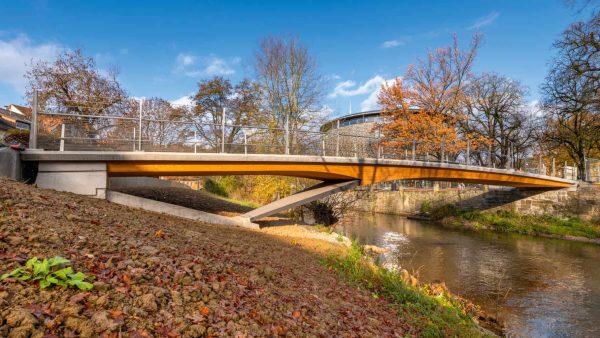 Bild 1: Die Lindachbrücke in Schwäbisch Hall überspannt den Kocher als elegantes Bauwerk. Die neue Fuß- und Radwegbrücke – eine Holz-Beton-Verbund-Konstruktion – bietet nun eine direkte Anbindung für Fußgänger und Radfahrer zwischen Bahnhof und der Unterwöhrd-Insel, auf der auch das Globe-Theater steht (im Hintergrund zu sehen), das damit ebenfalls den erforderlichen Zugang erhält. © Schaffitzel Holzindustrie – Jürgen Weller Fotografie