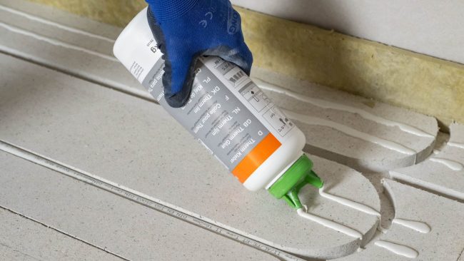 Der neu entwickelte Fermacell Therm Kleber reduziert den Montageaufwand nach Herstellerangaben erheblich. Statt wie bisher 70 Fixierungspunkte sind pro Abdeckplatte nur noch neun notwendig. Bezogen auf ein Projekt mit 120 Quadratmetern Fläche können durch den Einsatz des Klebers rund elf Stunden Arbeitszeit eingespart werden. Der deutlich dünnflüssigere Kleber lässt sich zudem einfach und ohne Druck ausbringen, was die Montage gerade bei niedrigeren Temperaturen weiter vereinfacht. © James Hardie Europe GmbH