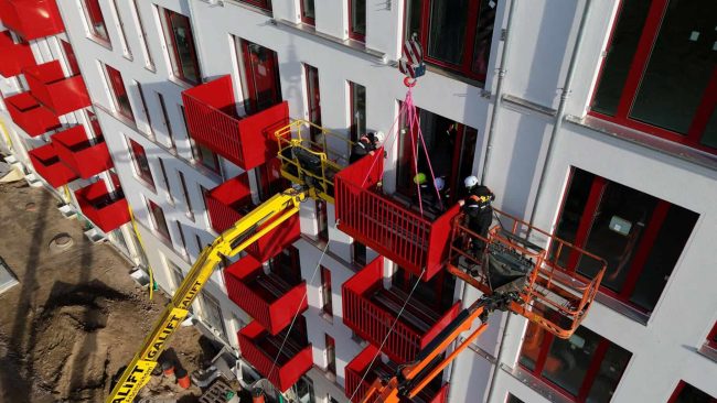 Die Module werden geliefert und montiert, dann wird das Gerüst gestellt, um die Fassade anzubringen und danach wieder abgerüstet. Anschließend können die Balkone bauzeitenflexibel sowie stützenfrei eingehoben und über eine einfache Schraubverbindung befestigt werden. © Schöck Bauteile GmbH