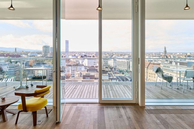 In den Attikageschossen unter den Flachdächern bieten Rundumverglasungen mit raumhohen Türen einen Blick auf die Stadt; im Neubau finden Angestellte hier oben informelle Aufenthaltsbereiche. © Zejlko Gataric, Zürich / Schüco International KG