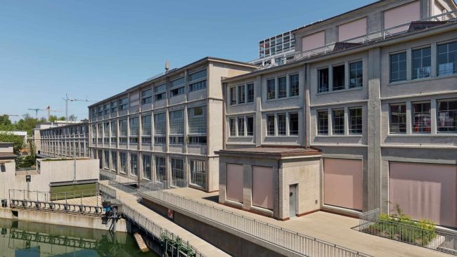 Östlich der Lorze bildet der langgestreckte Riegel mit den ehemaligen Papiermaschinenhallen die Kulisse für einen lebendigen neuen Stadtraum. Die Umnutzung zu Gewerbe, Kultureinrichtungen und Wohnungen übernahmen Boltshauser Architeken aus Zürich. © Damian Poffet