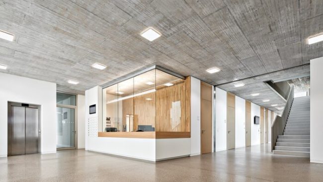 Abgeschottet und doch offen: Der Empfang ist vollverglast – mit einer beweglichen Scheibe kann ein persönlicher Kontakt hergestellt werden. © Schörghuber